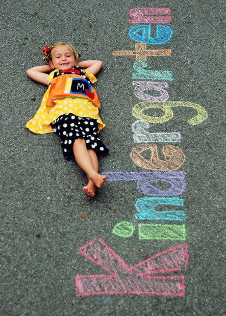 little girl laying on the driveway with Kindergarten written next to her 