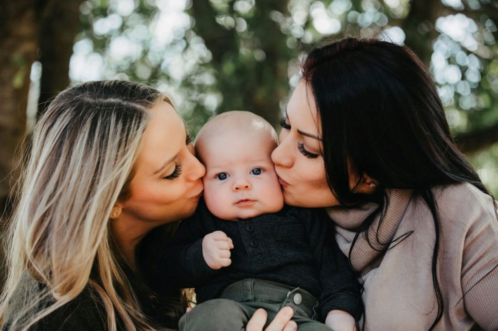 lesbian couple kissing their baby boy on the cheek 