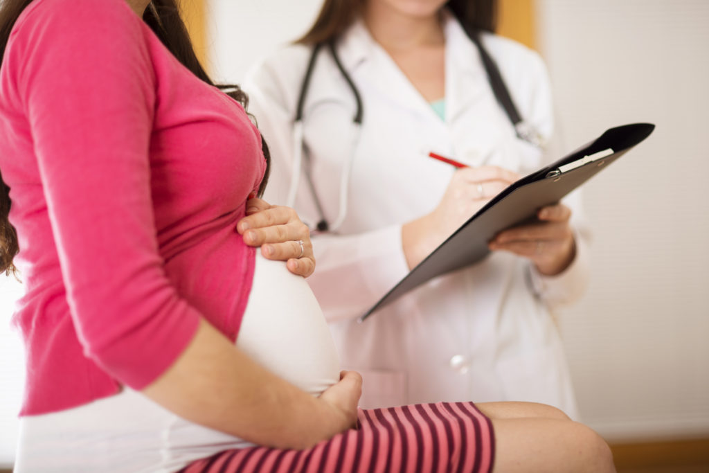 pregnant woman holding her belly at a doctors appointment 